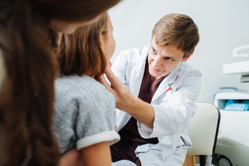 Obraz premium Little girl in being examined by friendly pediatrician, sitting on mom's lap