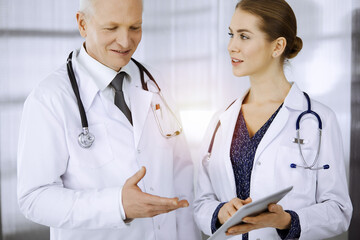 Elderly confident doctor and woman-physician discussing current disease therapy while standing in...
