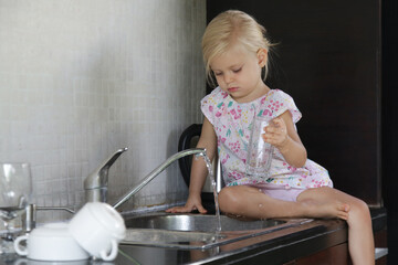 Child washing dishes in the kitchen. Cute two year old girl washes glass in sink. Early development, baby helps the parents. Chores for children.