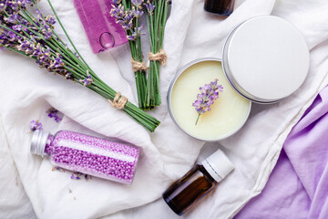 Obraz na płótnie Canvas Set lavender skincare cosmetics products. Natural spa beauty products fresh lavender flowers on fabric. Lavender essential oil bottle body butter massage oil cream soap bath beads gel liquid. Flat lay