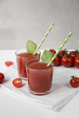 Two glasses with tomato juice stand on a light background, decorated with tubes and mint leaves, next to it are tomato slices