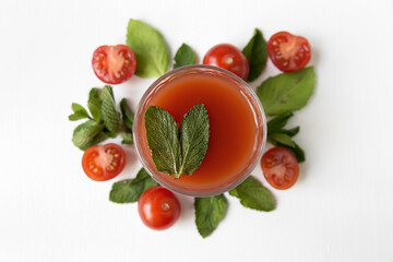   A glass with beautiful tomato juice on the background of tomatoes and herbs, close-up.
Beautiful composition of a glass with tomato juice, tomato, basil leaves and mint on a white background.