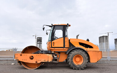 Vibro Roller Soil Compactor leveling soil at construction site. Excavator and vibration single-cylinder road roller during the construction of road. Road work project. Laying new asphalt