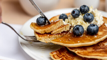 
Tasty breakfast. Freshly cooked pancakes with blueberries, honey and cottage cheese on a white plate. Close-up.