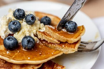 
Tasty breakfast. Freshly cooked pancakes with blueberries, honey and cottage cheese on a white plate. Healthy food.