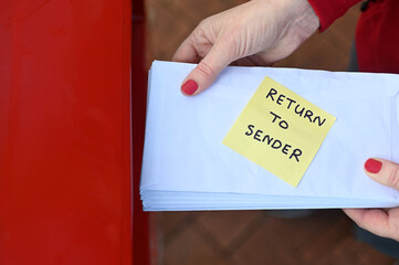 Woman sending return to sander letters in envelope in red mail box