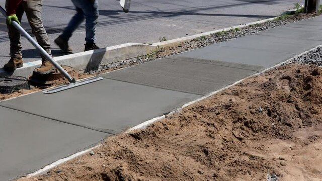 Construction mason building a screed coat cement a laborer floats a new concrete sidewalk