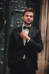 portrait of a stylish young groom in an old European town. man in a stylish suit with bow tie near old building. wedding day