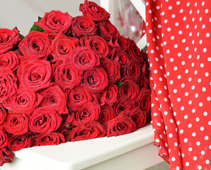 A bouquet of red roses and a red polka-dot dress on a white chair.
