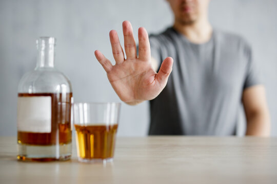 alcoholism concept - young man refusing glass of whiskey with open palm