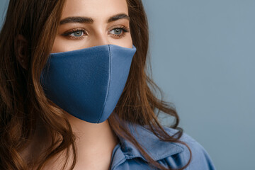Woman wearing stylish protective blue face mask. Young beautiful brunette model. Trendy Fashion...