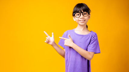 Portrait of young Asian girl smiled and point to copy space for text or products, Thai kid in violet shirt and wearing black glasses with happiness isolated in studio on orange background