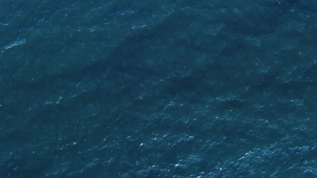 Texture of water surface of sea reflection of sun's rays. Sun glare on blue water aerial view from drone at low altitude on sunset summer. Motion of small waves. Sea idyll. Relax