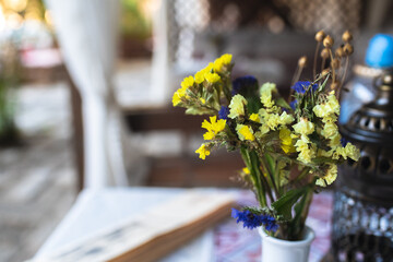 Small yellow flowers in a vase with oriental lantern on cafe table