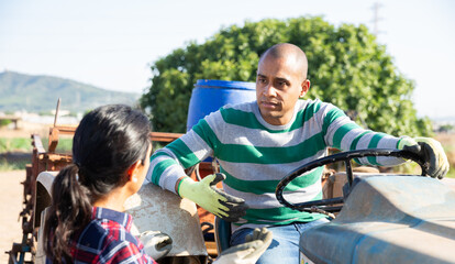 Fototapeta na wymiar Portrait of latino male farmer sitting on farm tractor and talking with woman