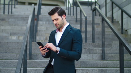 Closeup businessman laughing at street. Man using modern smartphone outside