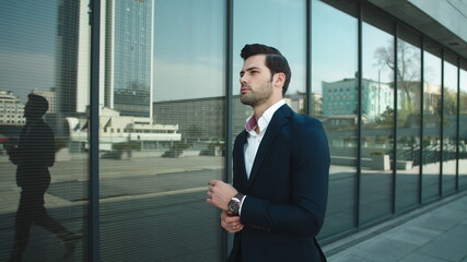 Portrait man checking time on watch. Businessman walking in suit at street