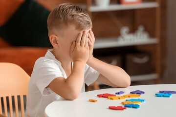 Sad little boy with autistic disorder doing puzzle at home