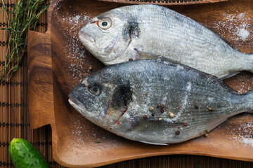 Two rainbow trout on a board, with herbs , ready for cooking.