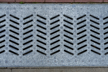 Close-up wide metal grating for rainwater drainage, mounted between concrete and paving stones.