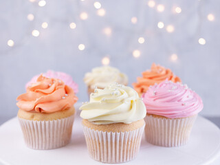 Cupcakes with pink, orange and white cream, selective focus on blurred lights background with copy space, closeup. Celebration concept.
