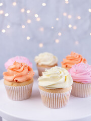 Cupcakes with pink, orange and white cream, selective focus on blurred lights background with copy space, closeup. Celebration concept.