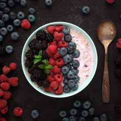 Oatmeal with blueberries, raspberries, blackberries in a bowl with a vintage spoon for breakfast. Healthy breakfast. Dark background, top view.