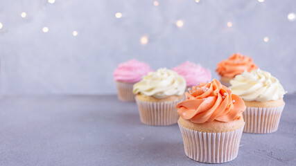 Cupcakes with pink, orange and white cream, selective focus on blurred lights background with copy space, banner. Celebration concept.