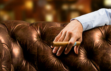 Mano de hombre con puro sobre chaise longe de cuero marrón. Man's hand with cigar on brown leather chaise longue.