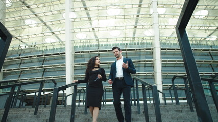 Business man and woman talking together. Couple walking in black suits outdoors