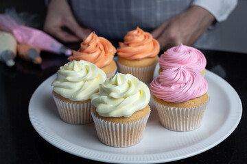 Fresh cupcakes with pink, orange and white cream on white plate, closeup. Home baking concept.