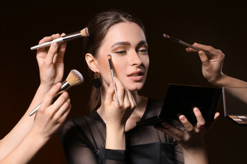 Fototapeta premium Makeup artists working with beautiful young woman on dark background