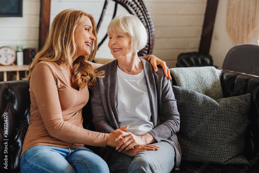 Wall mural Senior mother with adult daughter hugging each other on sofa in living room