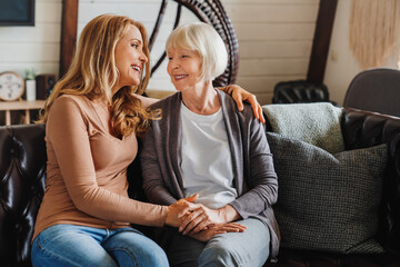 Senior mother with adult daughter hugging each other on sofa in living room