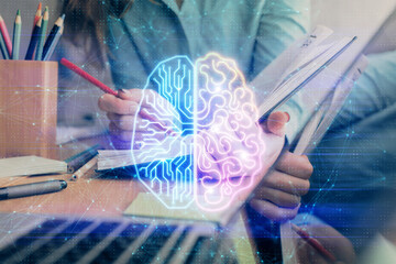 Double exposure of woman's writing hand on background with brain hud. Concept of learning.