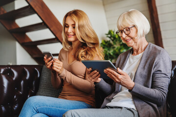 Senior women using digital tablet and middle aged woman, her daughter, mobile phone while relaxing...