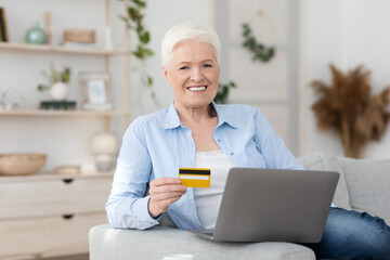 Online Shopping. Smiling Elderly Woman Posing With Laptop And Credit Card At Home