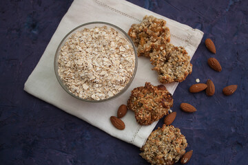 Oatmeal in a bowl on white serviette with oatmeal cookies and almond around it. Violet grunge background
