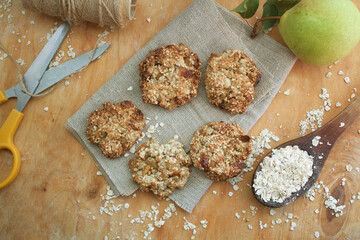 Oatmeal cookies on the piece of sackcloth with wooden spoon, 
scissors and pear. Wooden background
