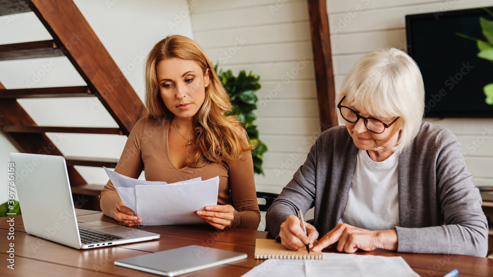 Wall mural senior woman with help of her daughter making bills at home