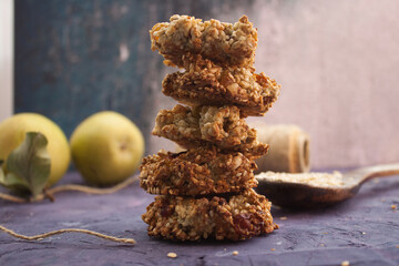 Homemade oatmeal cookies folded in a pile on violet grunge background with pears and wooden spoon behind
