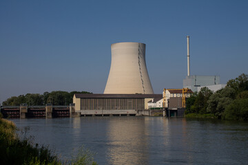 The cooling tower of a nuclear power plant is reflected in a river. In front of it is a hydropower plant.