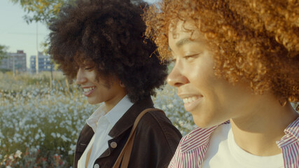 closeup side view portrait of two mixed race black woman walking in the park smiling in morning sunlight