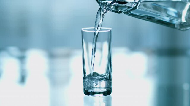 Pure drinking water is poured into a glass cup on a light background, close-up