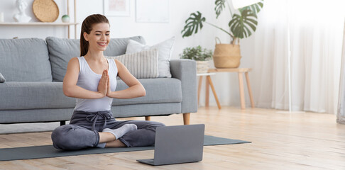 Peaceful young woman meditating at home, using laptop