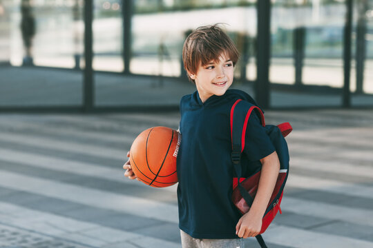 Portrait of a beautiful boy in sports uniform with a backpack and a basketball. The boy smiles and holds the ball in his hands. Training, education, physical education
