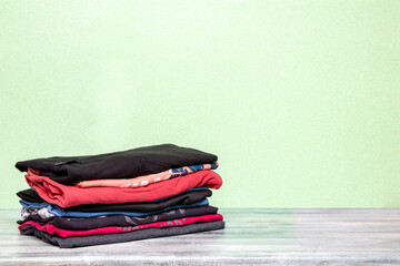 Pile of folded cotton t-shirts or shirts on a bright table with space for your display product montage on a light gree glitter sparkle background. Summer fashion.