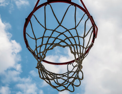 Close up with a basketball hoop against blue and cloudy sky.