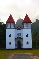 Moorea, French Polynesia - July 07 2014: Catholic church, red and white with mountain in background, in Haapiti Moorea French Polynesia