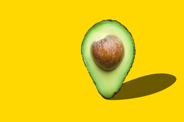 Raw ripe halved avocado with pit imitating map pointer with drop shadow on yellow background. Creative food poster banner for vegan healthy oil diet concept - obrazy, fototapety, plakaty
